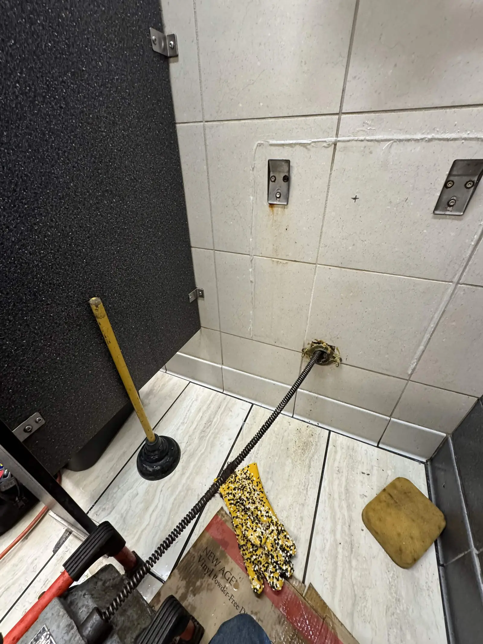 A drain cleaning cable entering a pipe in a commercial restroom.