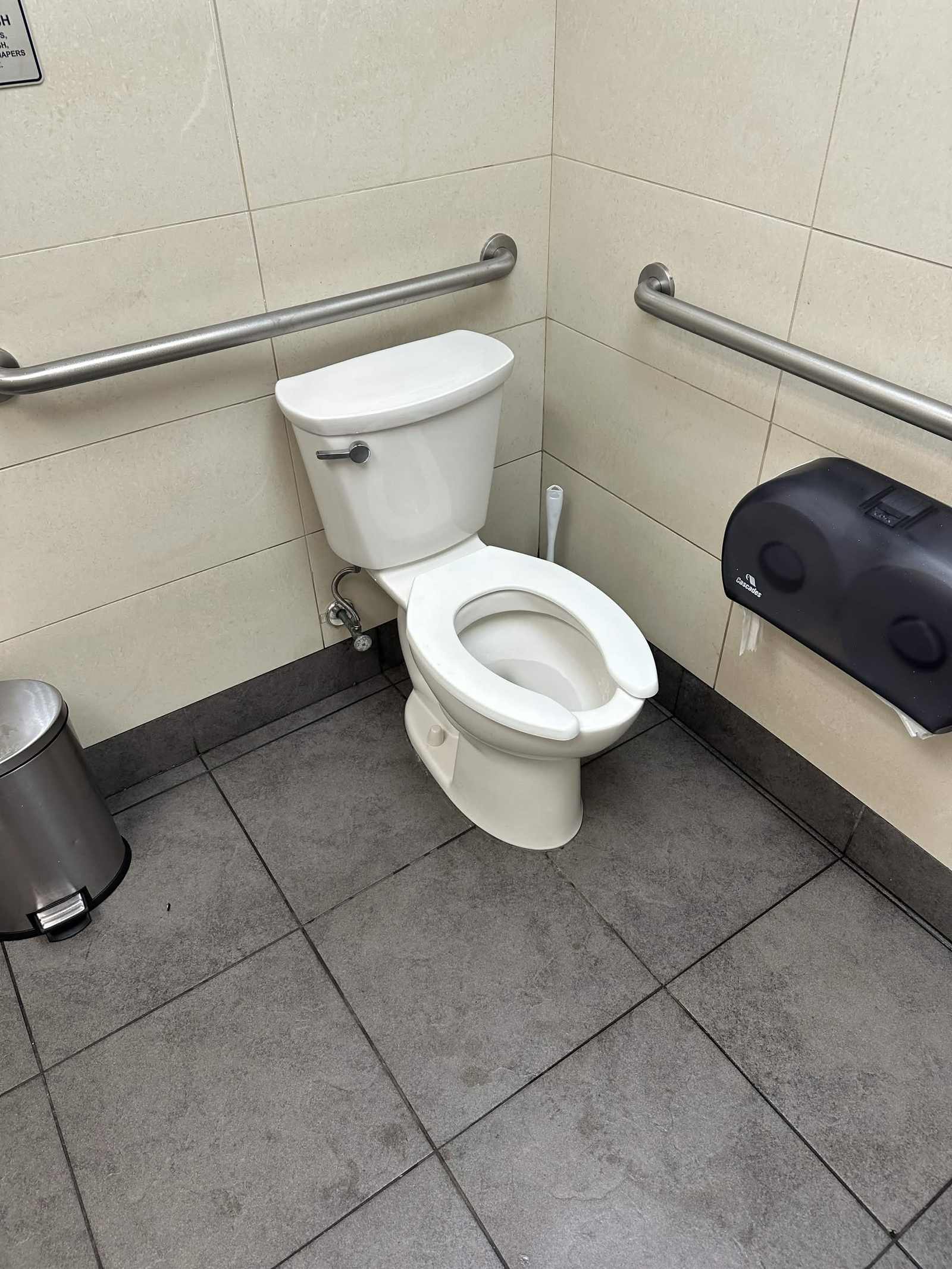White toilet installed beside grab bars in a tiled commercial restroom.