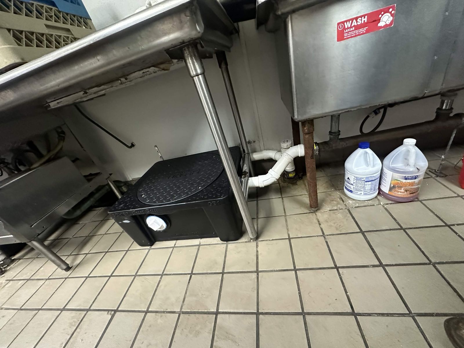 Grease trap under a restaurant's three-compartment sink.